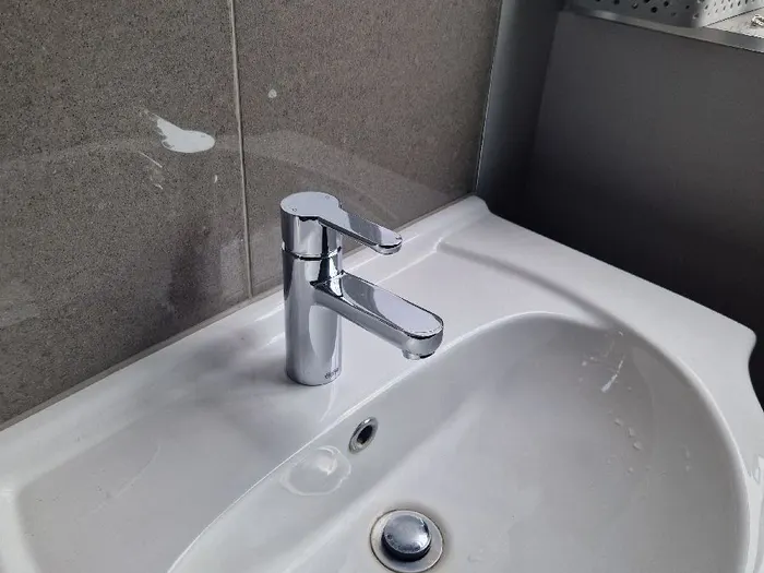 Basin with a chrome mixer tap against grey tiles