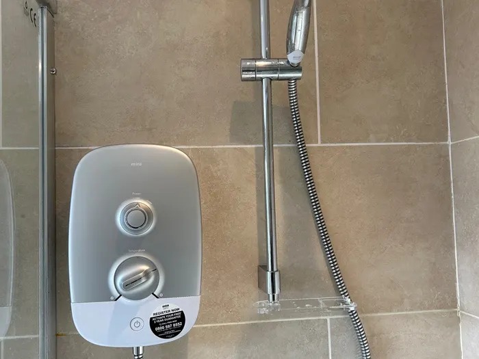 Electric shower fitted in a tidy tiled cubicle with a riser rail